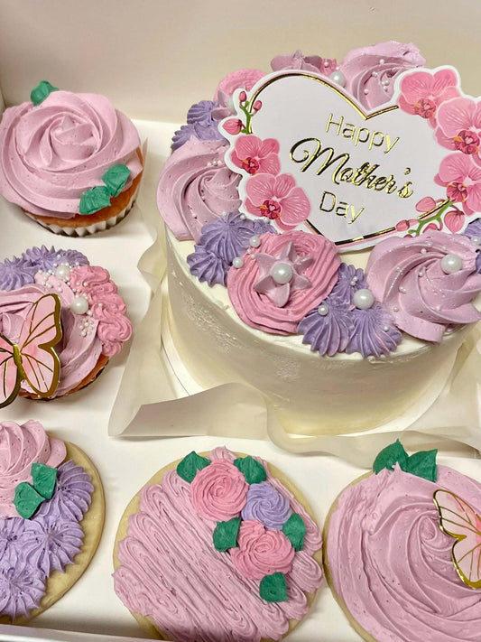 Decorative cake and cookies with pink and purple icing, featuring 'Happy Mother's Day' text.