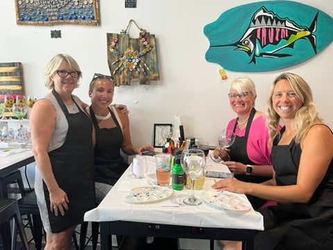 Four women in a restaurant setting with a colorful fish art piece on the wall.
