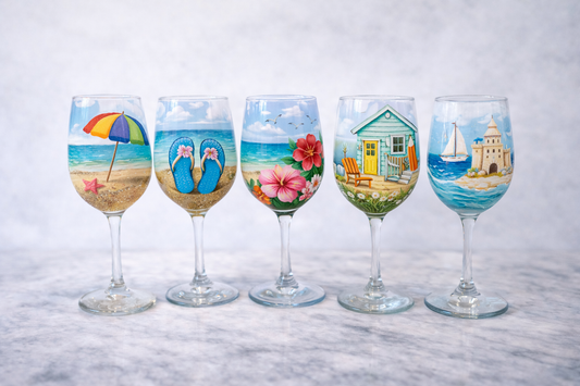 Set of five decorated wine glasses with beach-themed designs on a marble surface.