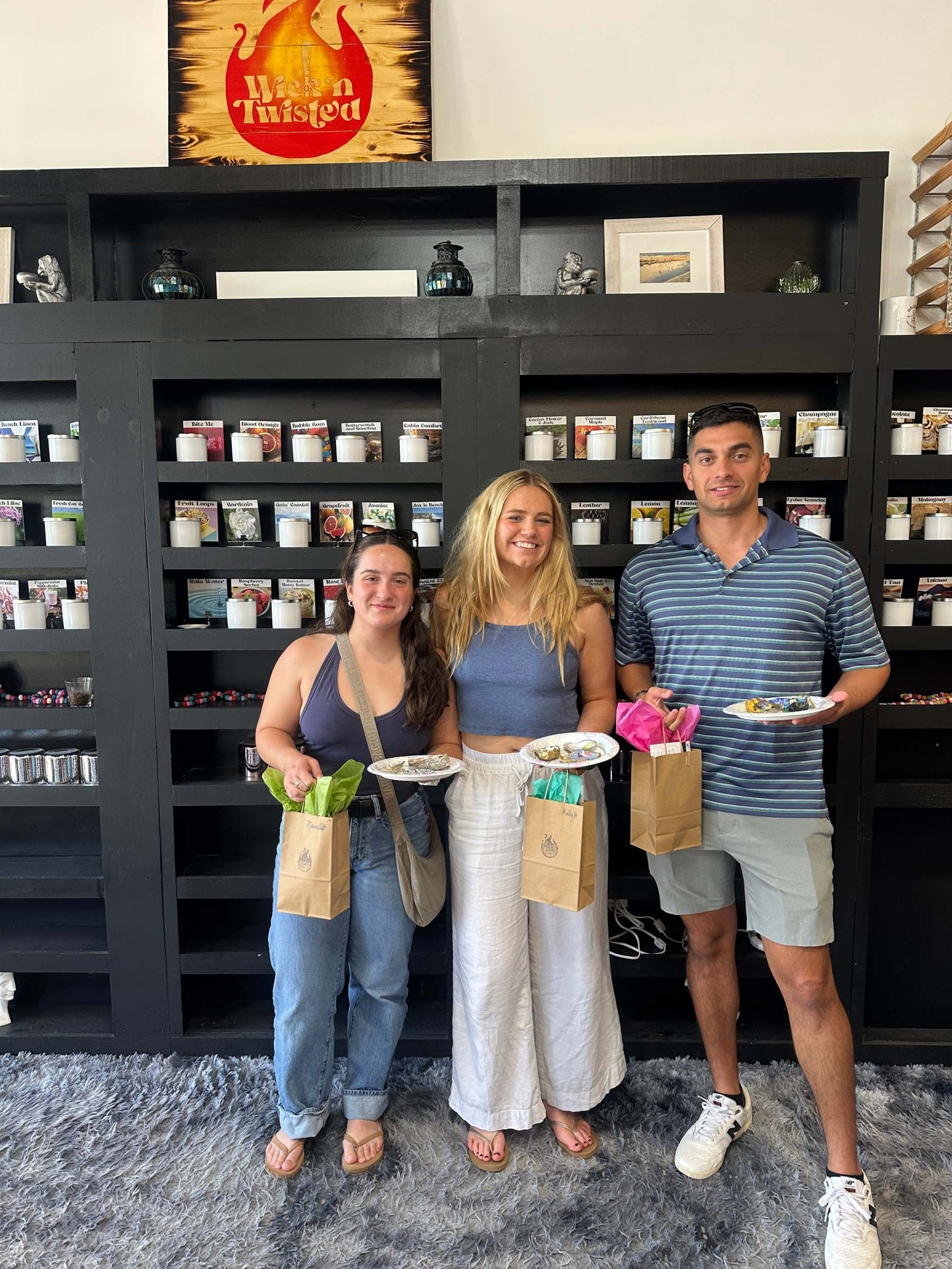 Three people standing in a store holding plates and bags, with shelves and decor in the background.